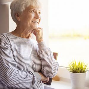 An older women looking out the window smiling and thinking