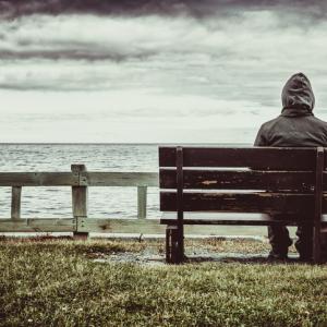 A person sitting on a park bench looking out at the ocean