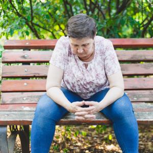 A mature aged woman sitting alone and looking down on a park bench