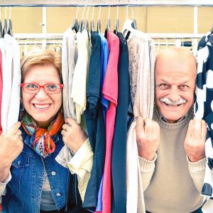 Happy senior couple smiling through clothing rack